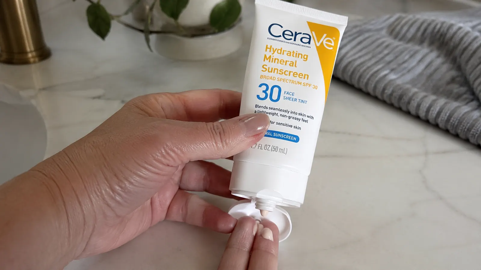 Hand dispensing CeraVe Hydrating Mineral Sunscreen from the tube onto fingertips before blending