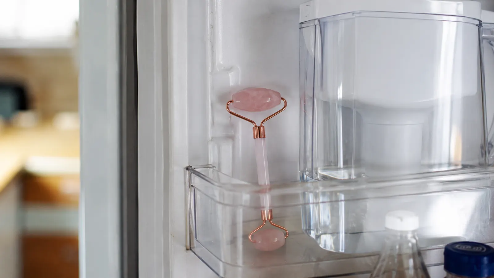 Rose quartz facial roller resting in the door shelf of a refrigerator next to a water pitcher