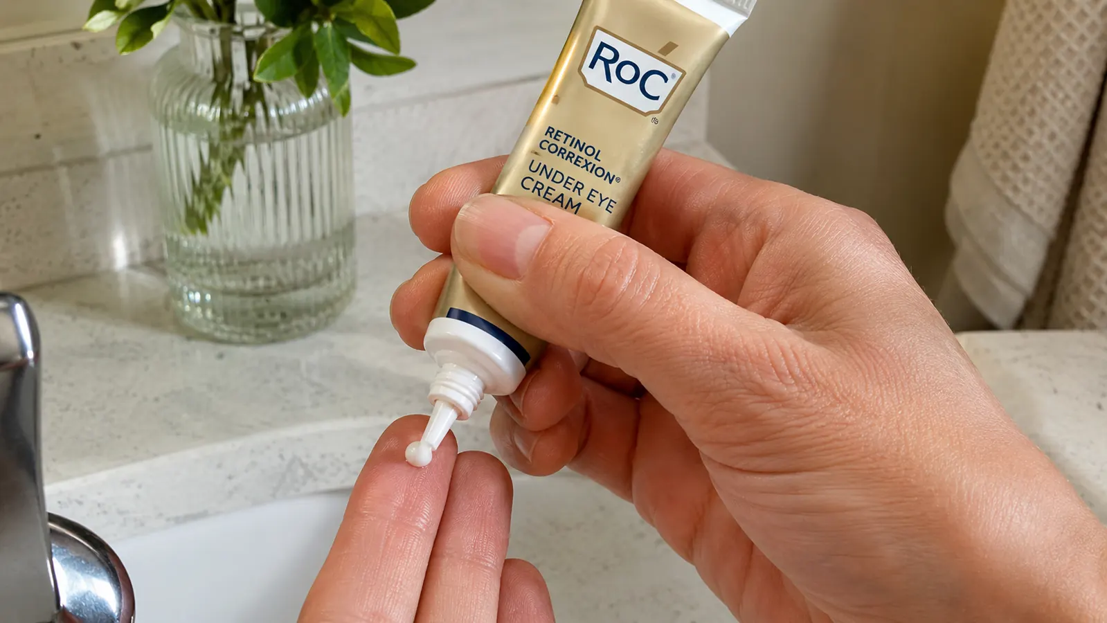 Close-up of a hand dispensing a small rice grain amount of RoC Retinol Correxion Under Eye Cream onto a ring finger