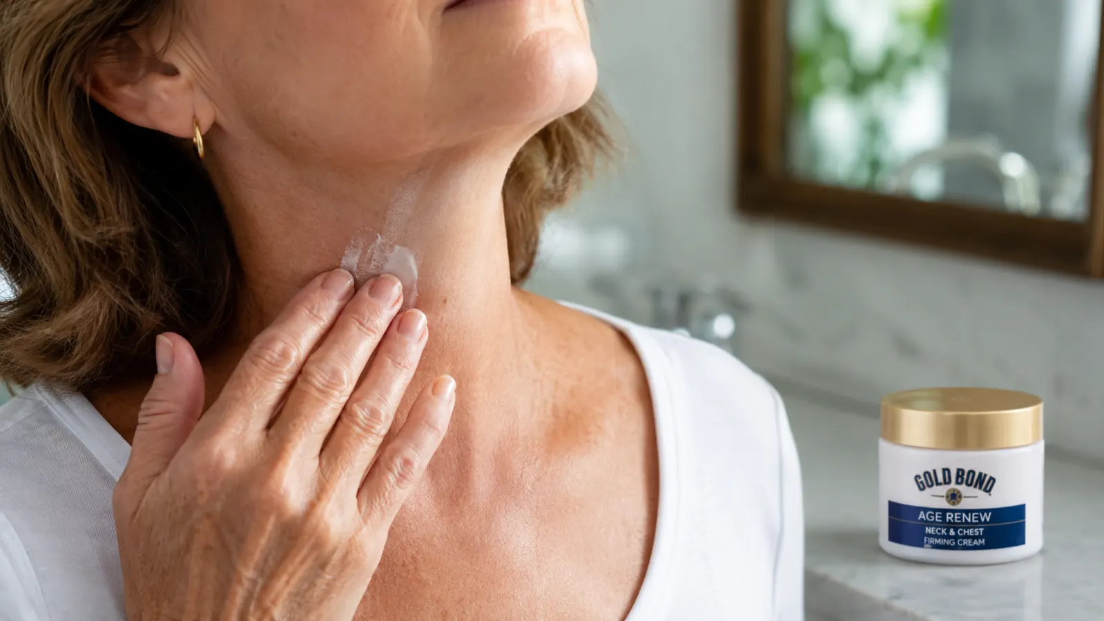 Hand applying Gold Bond Age Renew Neck & Chest Firming Cream in upward strokes from the collarbone toward the jaw