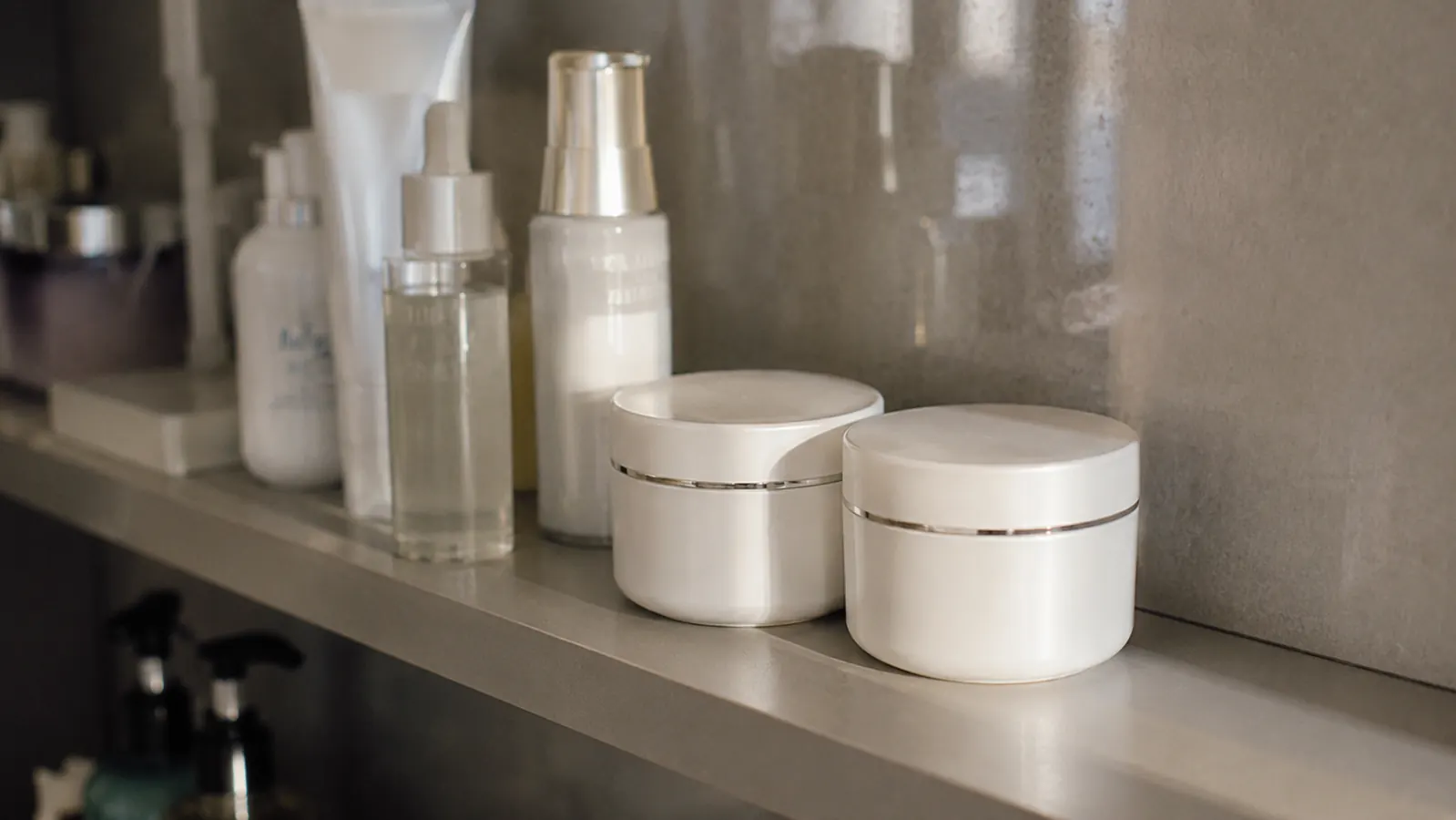 Two jars of neck and chest firming cream stored upright on a bathroom shelf away from a steamy shower
